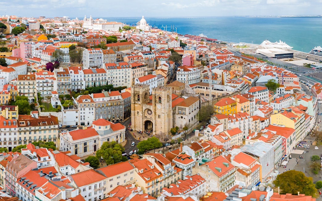 Aerial view of Se de Lisboa and surrounding Lisbon rooftops near the waterfront.