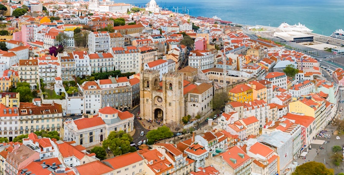 Aerial view of Se de Lisboa and surrounding Lisbon rooftops near the waterfront.