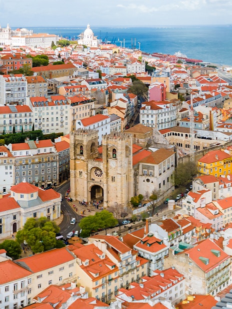 Aerial view of Se de Lisboa and surrounding Lisbon rooftops near the waterfront.