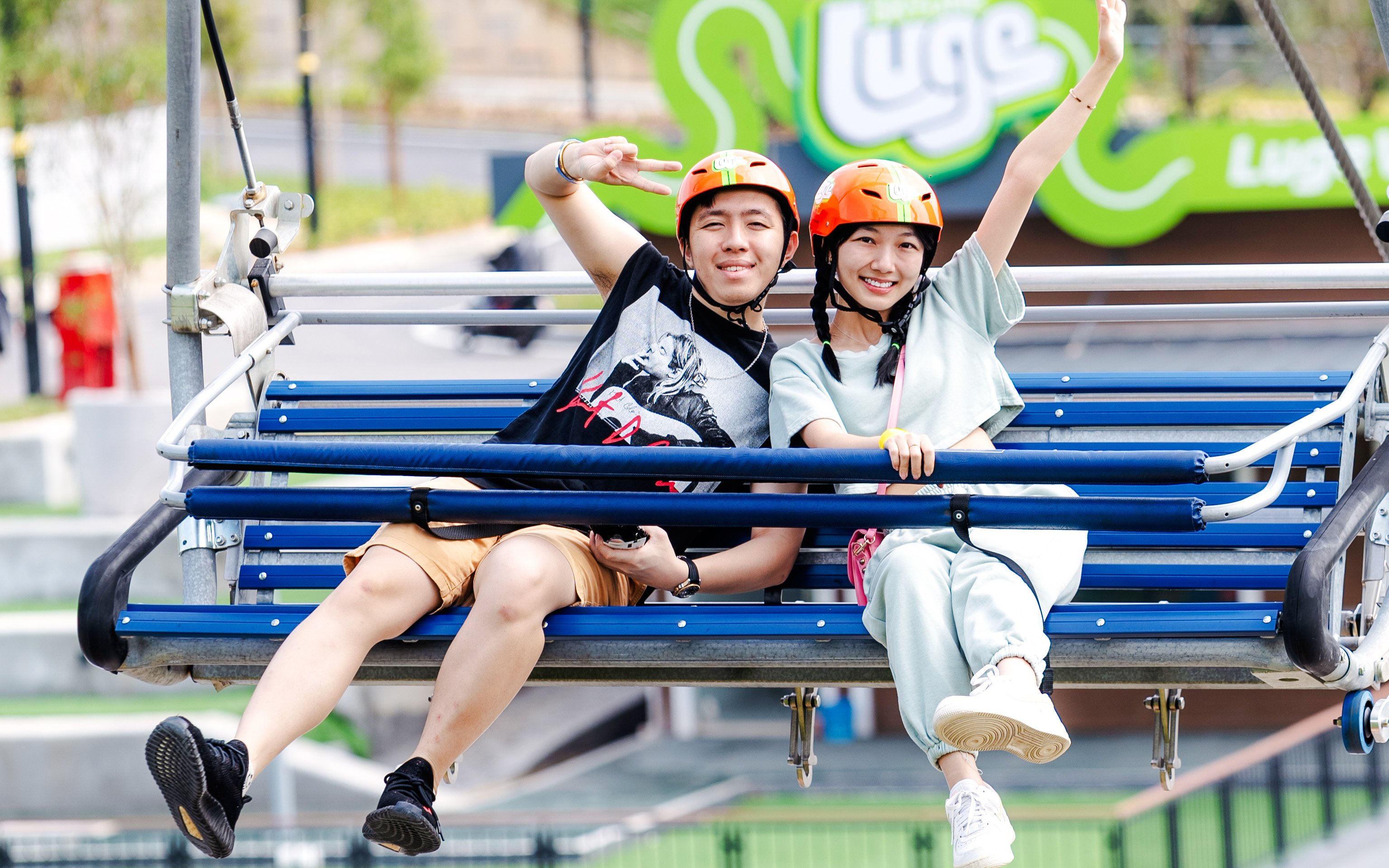 Two people on a chairlift at Skyline Luge, wearing helmets and smiling.