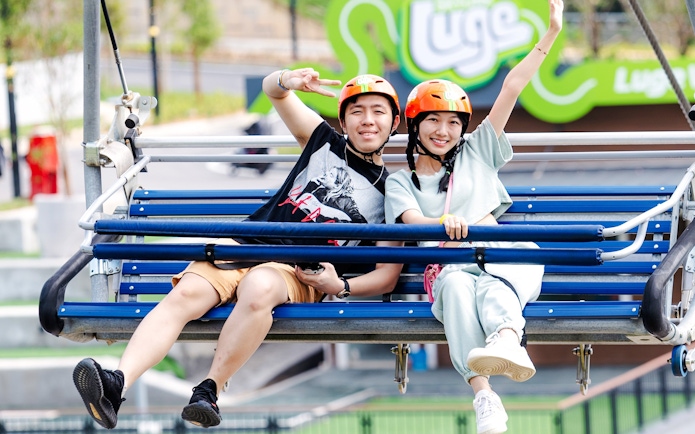 Two people on a chairlift at Skyline Luge, wearing helmets and smiling.