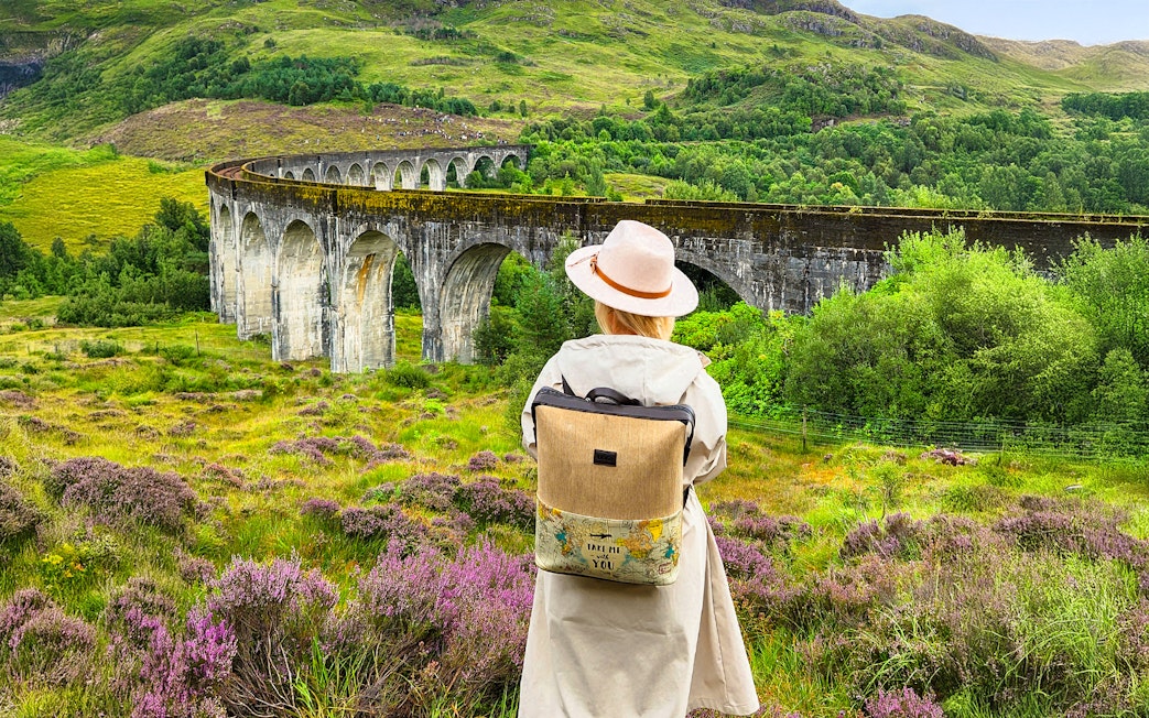 Guest standing near Glenfinnan Viaduct in Scotland, surrounded by lush greenery.