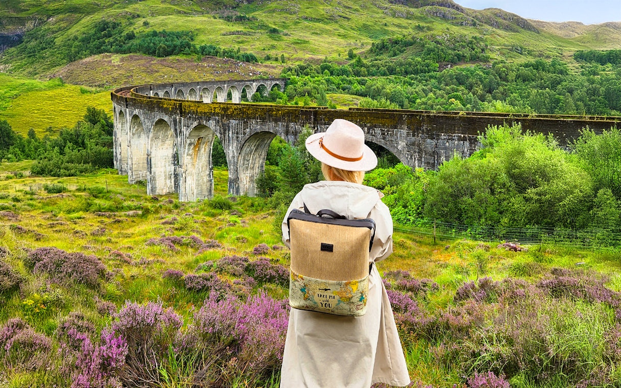Guest standing near Glenfinnan Viaduct in Scotland, surrounded by lush greenery.