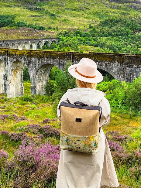 Guest standing near Glenfinnan Viaduct in Scotland, surrounded by lush greenery.