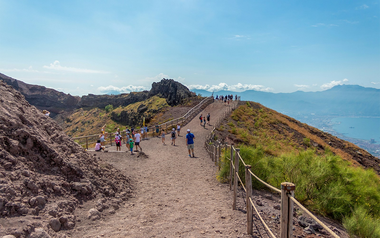 Hikers walking along a trail on Mount Vesuvius with views of the surrounding landscape.