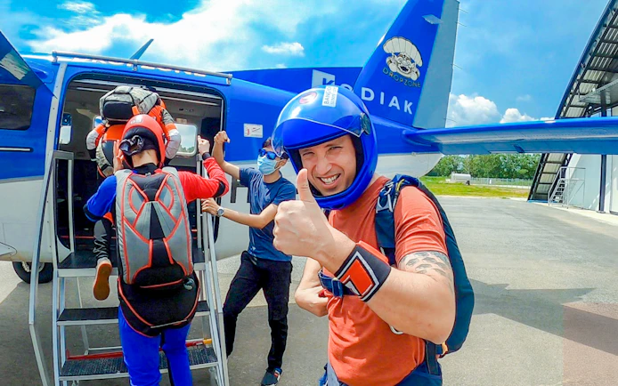 Tourists boarding a skydive plane, one giving a thumbs up, at a dropzone.