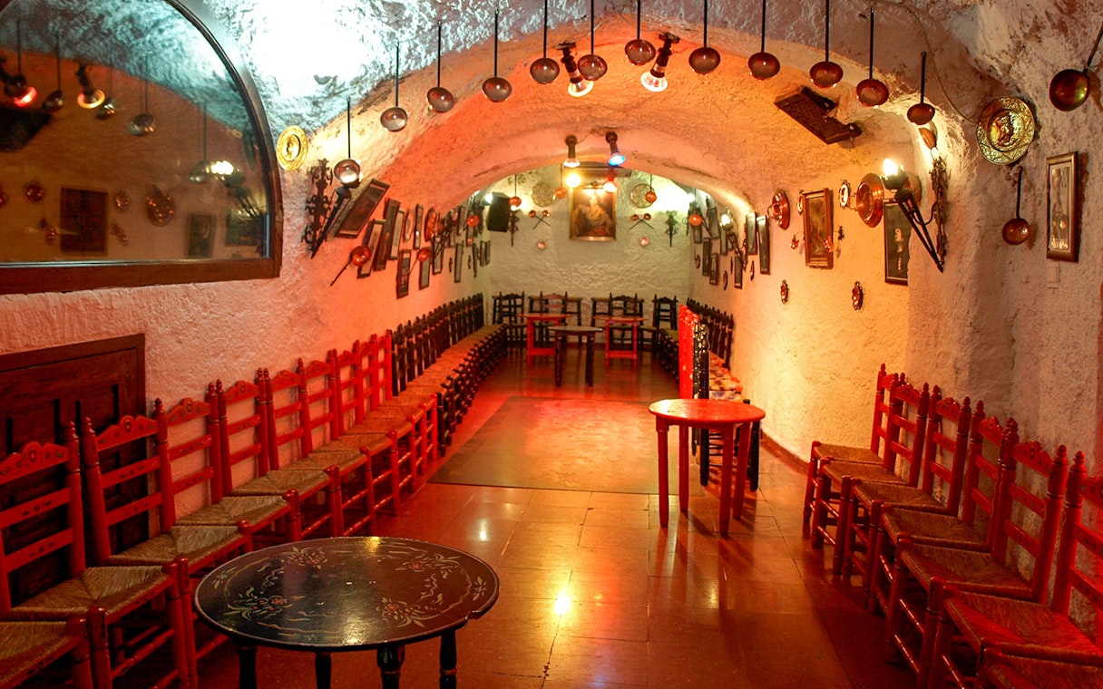 Flamenco Cuevas Los Tarantos performance area with red chairs and rustic decor.