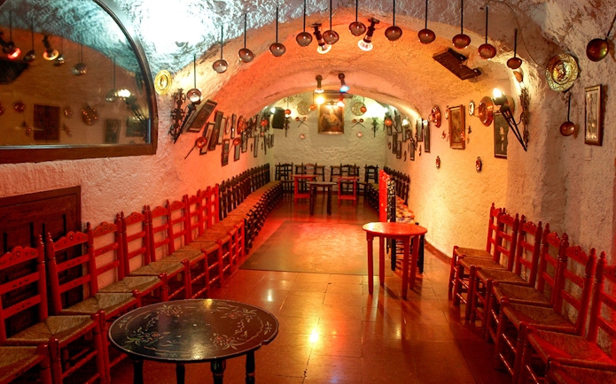 Flamenco Cuevas Los Tarantos performance area with red chairs and rustic decor.