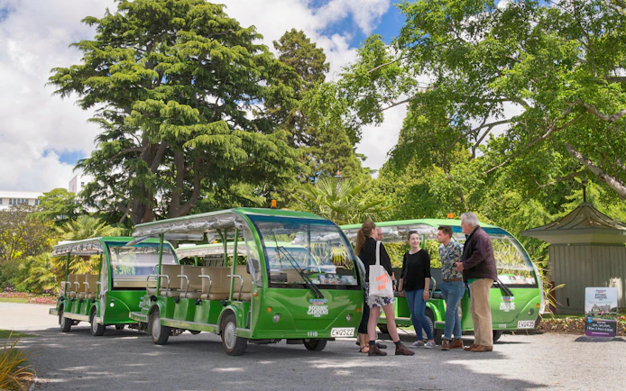 Tourists gather near green shuttle carts at Christchurch Botanic Gardens.