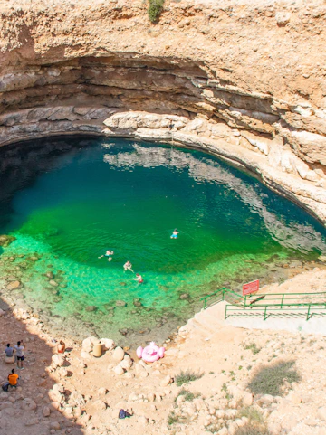 Swimmers enjoying the turquoise waters of Bimmah Sinkhole, Oman.