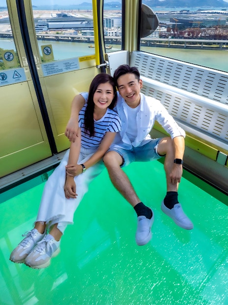 Couple enjoying Ngong Ping 360 cable car with glass floor, Hong Kong view.