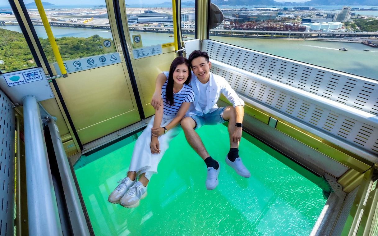 Couple enjoying Ngong Ping 360 cable car with glass floor, Hong Kong view.
