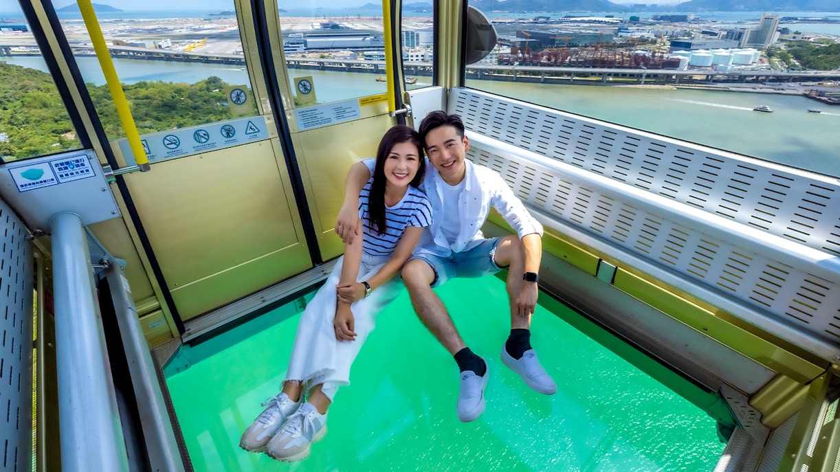 Couple enjoying Ngong Ping 360 cable car with glass floor, Hong Kong view.