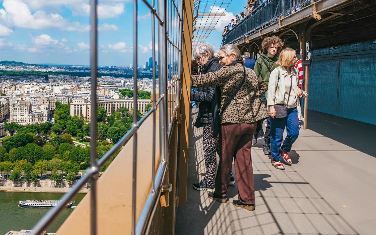 Visitors on Eiffel Tower viewing platform overlooking Paris during guided tour.
