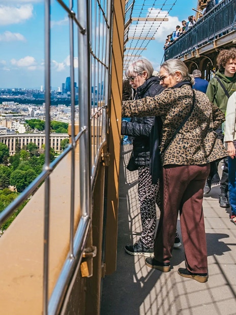 Visitors on Eiffel Tower viewing platform overlooking Paris during guided tour.