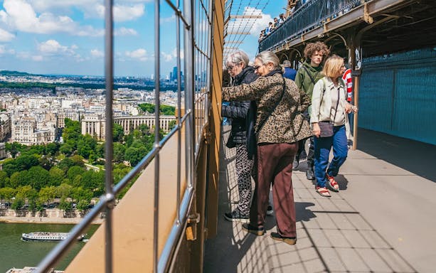 Visitors on Eiffel Tower viewing platform overlooking Paris during guided tour.