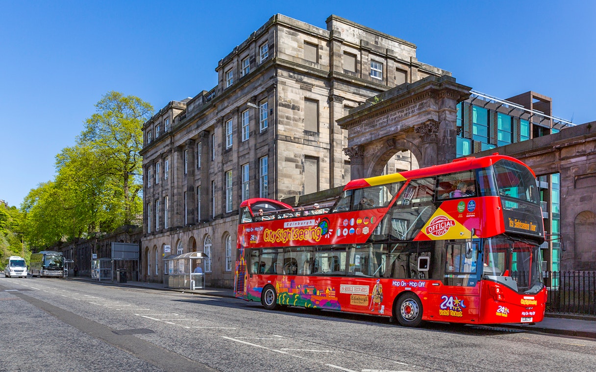 Edinburgh sightseeing bus in front of historic building on a sunny day.