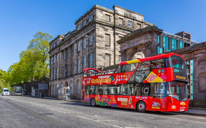 Edinburgh sightseeing bus in front of historic building on a sunny day.