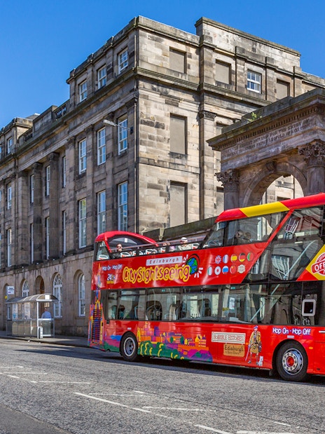 Edinburgh sightseeing bus in front of historic building on a sunny day.