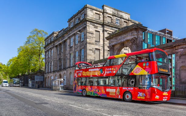 Edinburgh sightseeing bus in front of historic building on a sunny day.