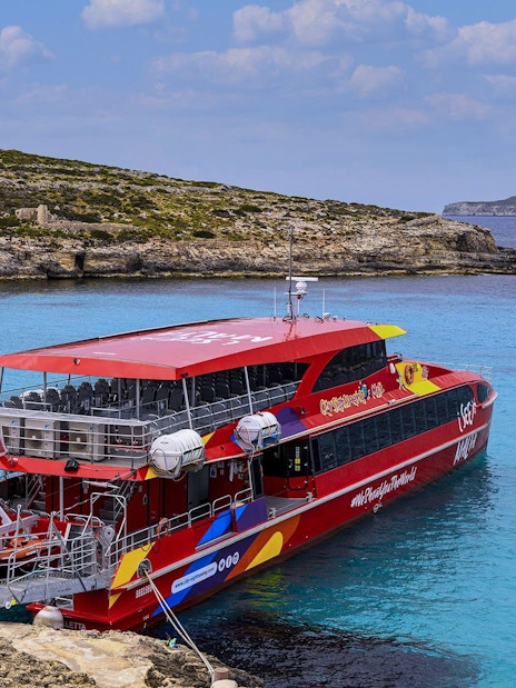 Catamaran docked in clear blue waters of Malta with rocky coastline in the background.