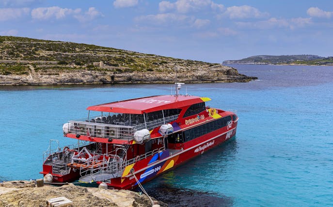 Catamaran docked in clear blue waters of Malta with rocky coastline in the background.