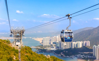 Ngong Ping Cable Car over Lantau Island with cityscape and mountains in the background.