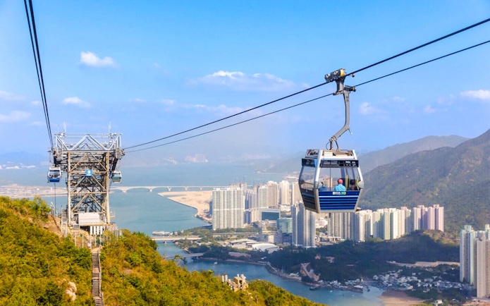Ngong Ping Cable Car over Lantau Island with cityscape and mountains in the background.