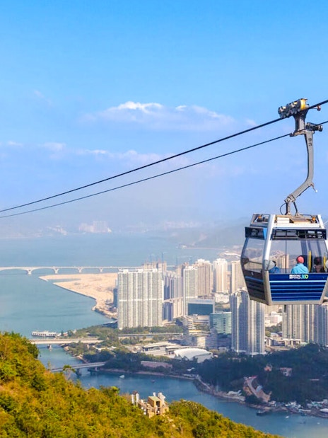 Ngong Ping Cable Car over Lantau Island with cityscape and mountains in the background.