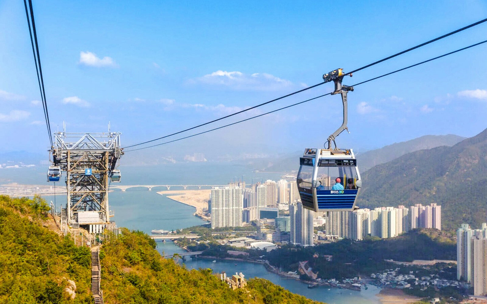 Ngong Ping Cable Car over Lantau Island with cityscape and mountains in the background.