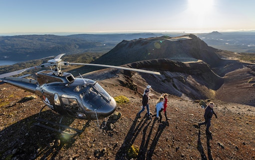 Helicopter landing on Mount Tarawera with tourists walking on volcanic terrain, New Zealand.