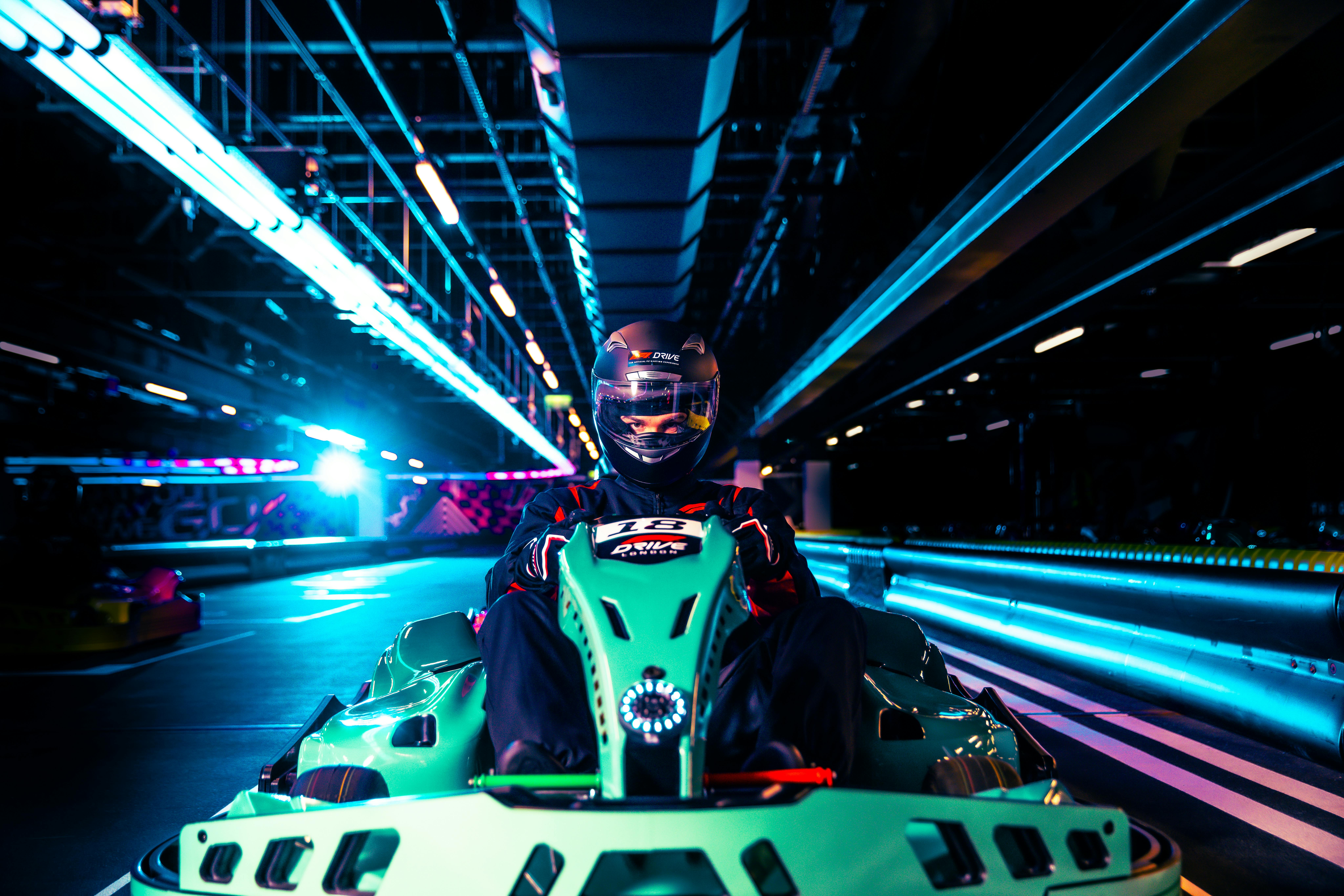 Person driving a go-kart on an indoor track with neon lights.