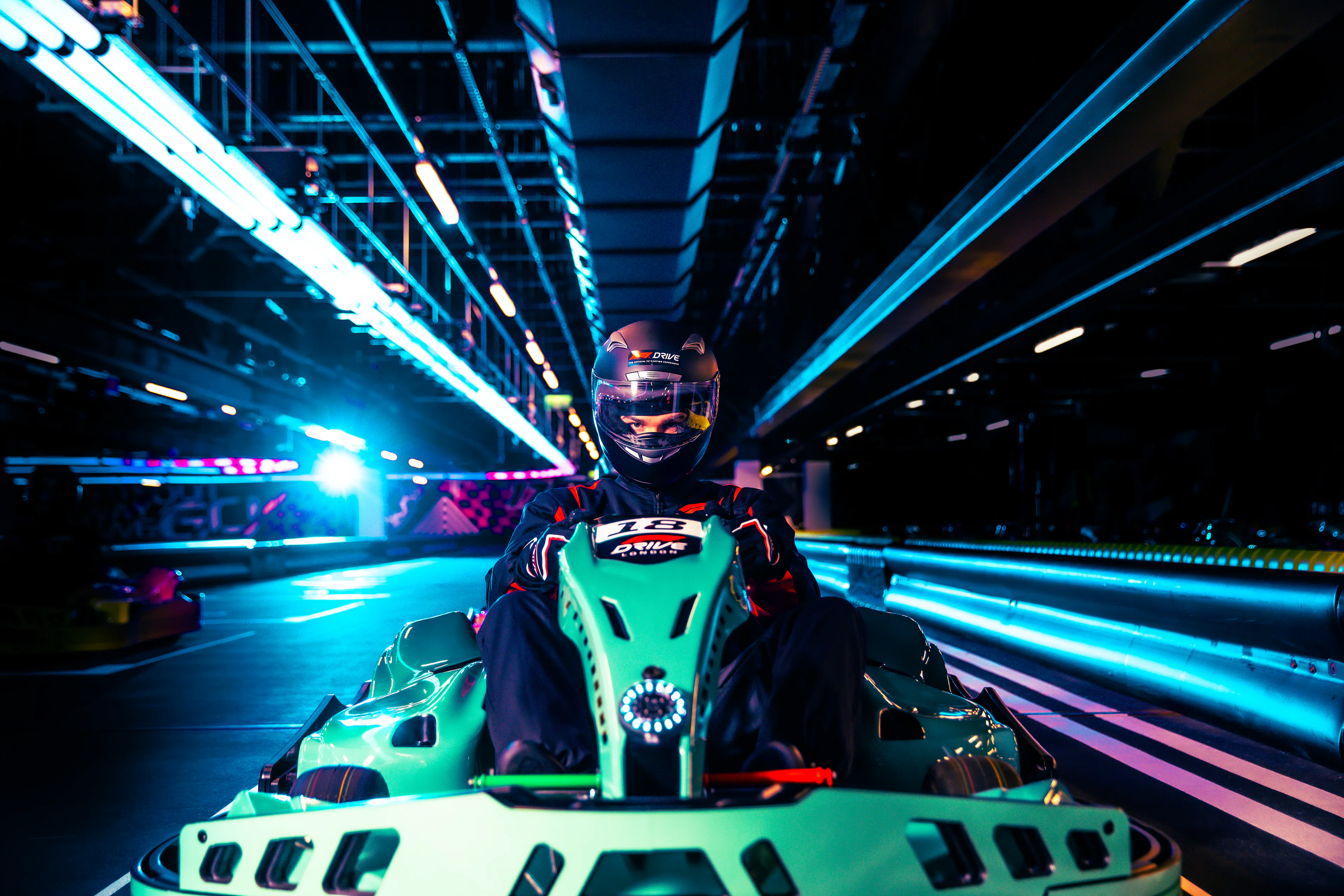 Person driving a go-kart on an indoor track with neon lights.