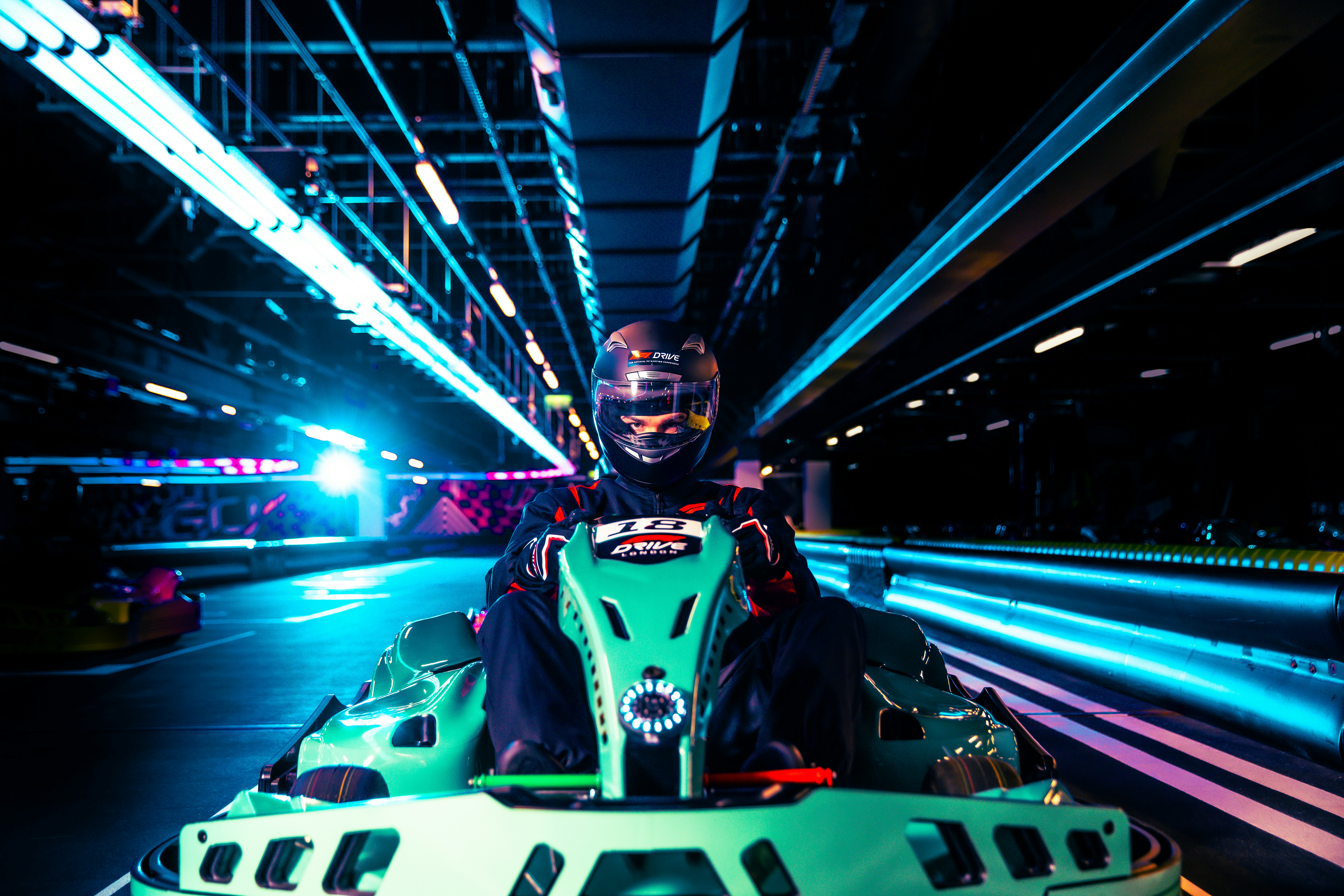 Person driving a go-kart on an indoor track with neon lights.