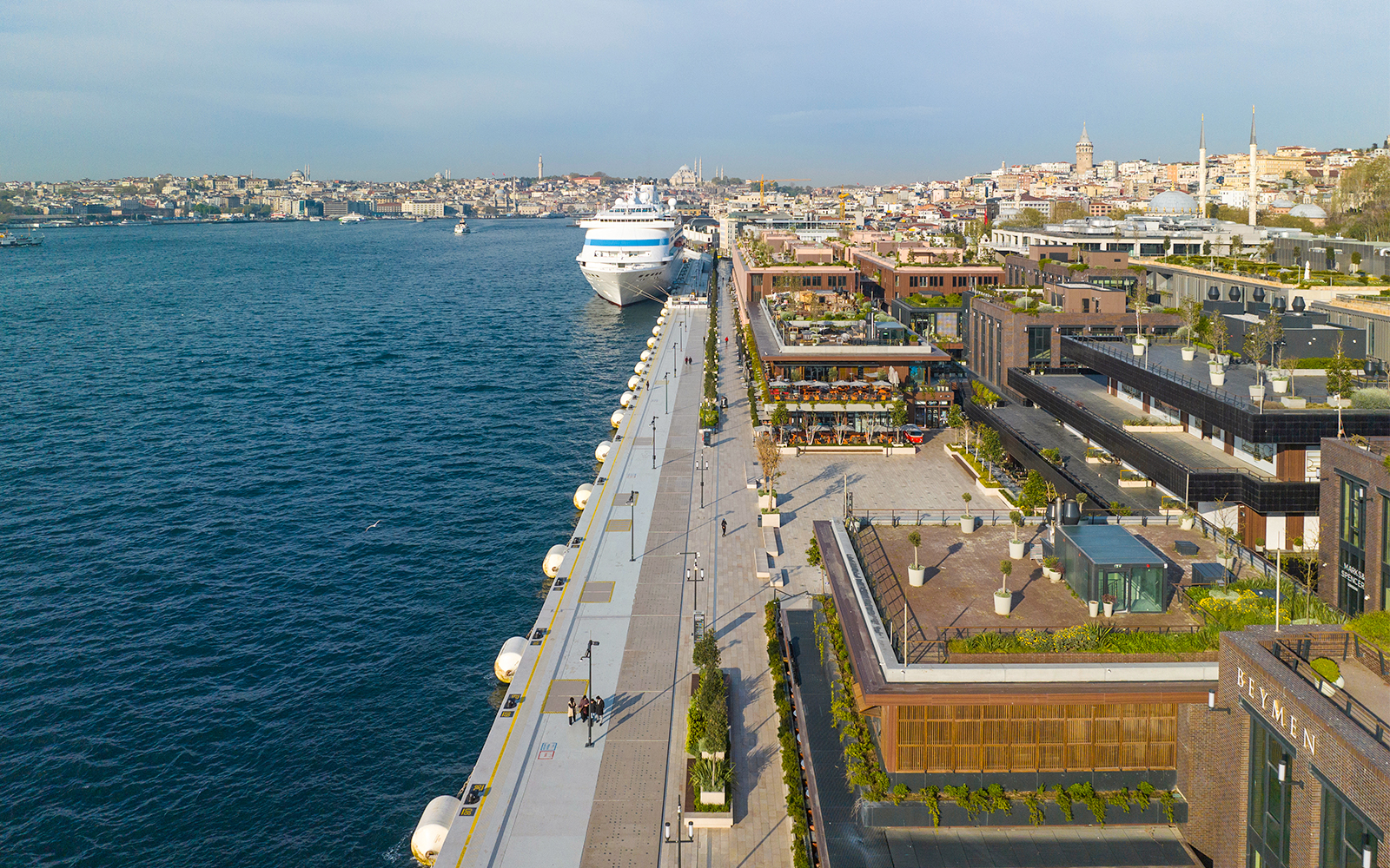 Galataport cruise liner docked at Bosphorus with adjacent shopping mall and cityscape.