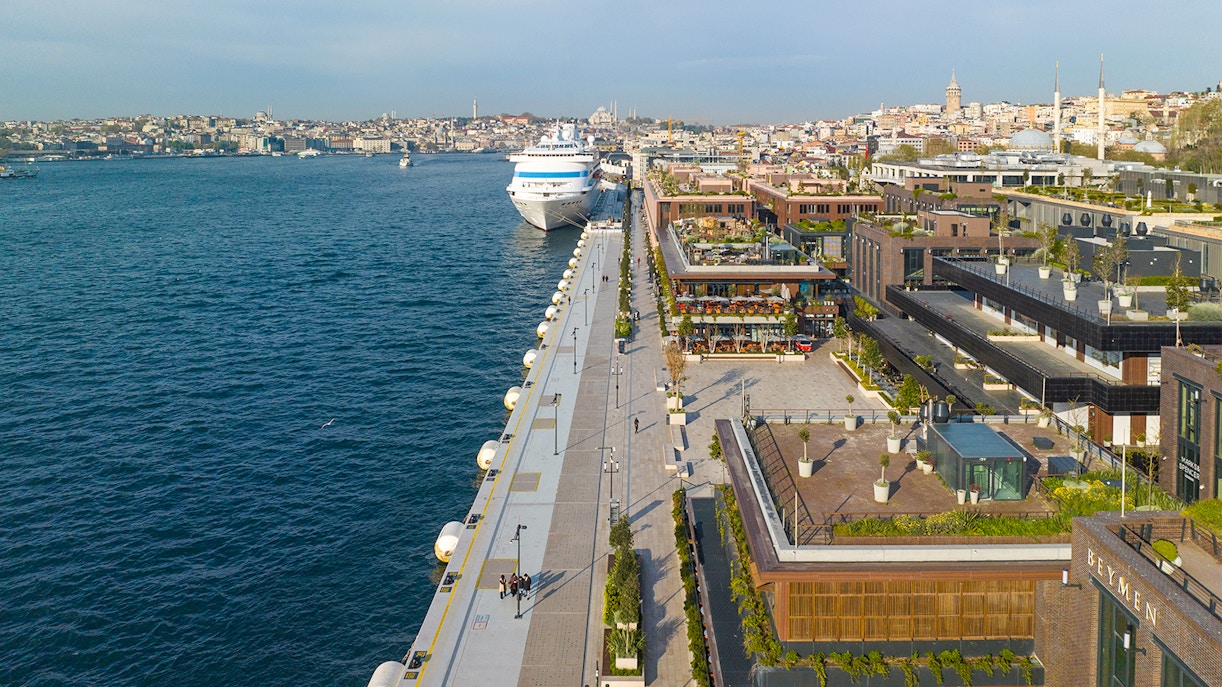 Galataport cruise liner docked at Bosphorus with adjacent shopping mall and cityscape.