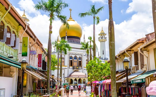 Sultan Mosque in Kampong Gelam, Singapore, with vibrant market stalls and palm trees.