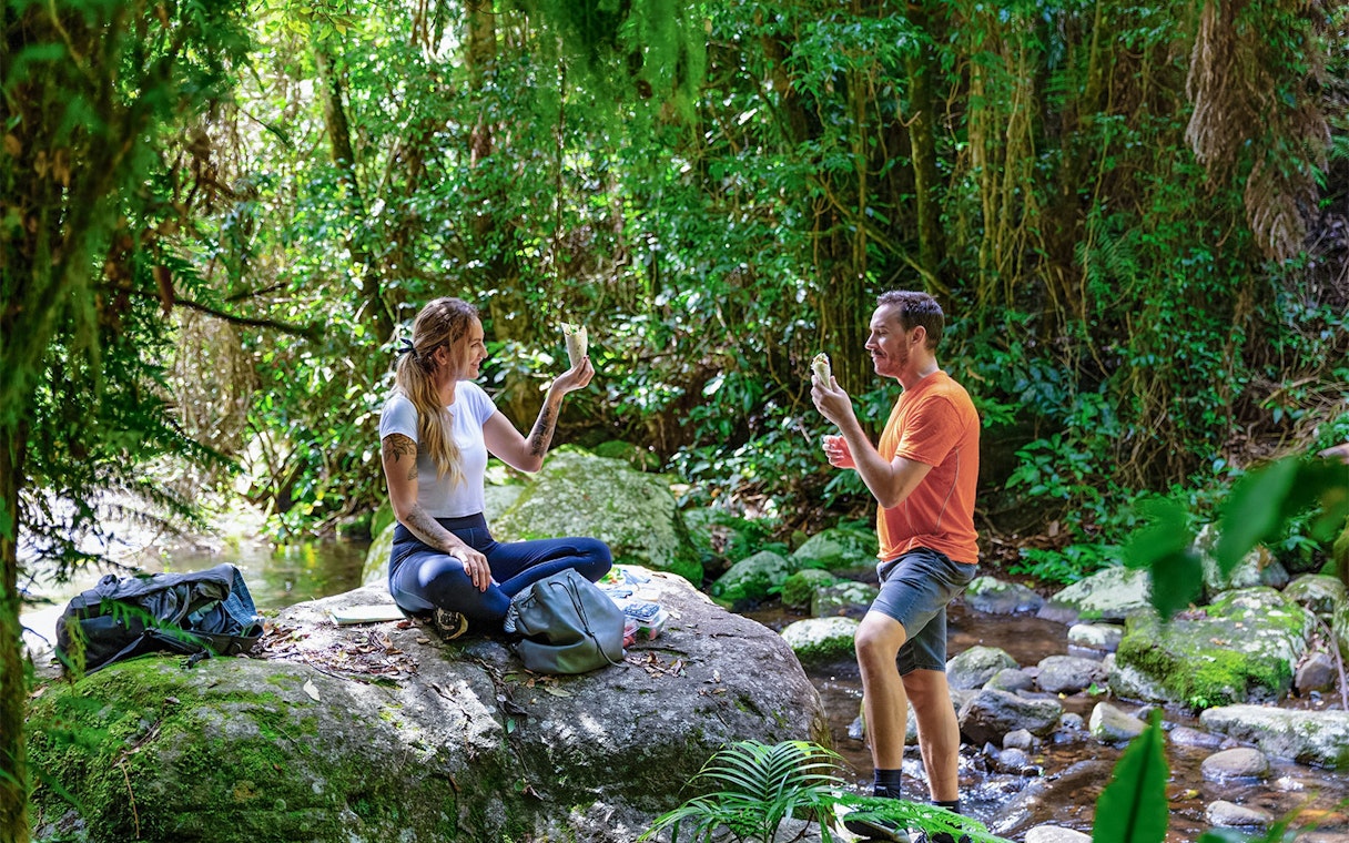 Couple enjoying a meal on a rock during a guided Daintree Rainforest tour.