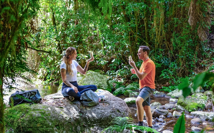 Couple enjoying a meal on a rock during a guided Daintree Rainforest tour.