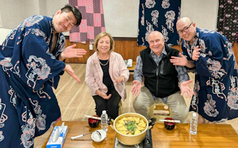 Former sumo wrestlers with guests enjoying chanko meal in Tokyo experience.