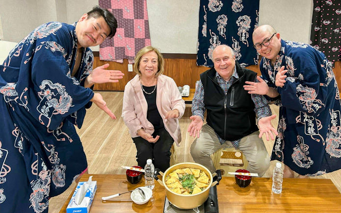 Former sumo wrestlers with guests enjoying chanko meal in Tokyo experience.