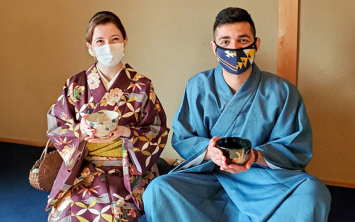 Two people in traditional attire holding tea bowls during a tea ceremony in Kyoto.