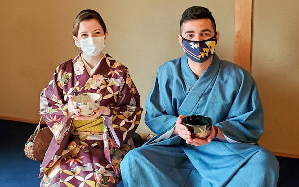 Two people in traditional attire holding tea bowls during a tea ceremony in Kyoto.