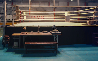 Boxing ring with desk and chairs in an indoor gym setting.