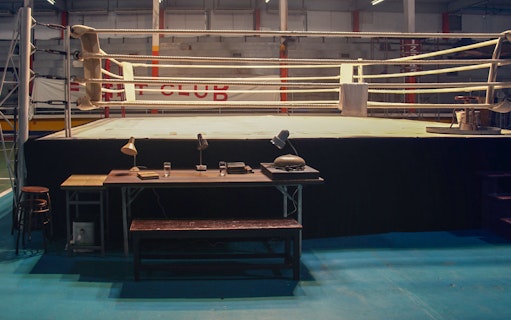 Boxing ring with desk and chairs in an indoor gym setting.