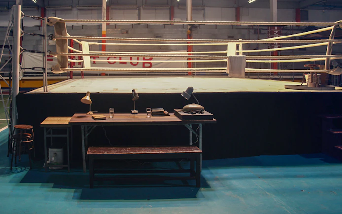 Boxing ring with desk and chairs in an indoor gym setting.