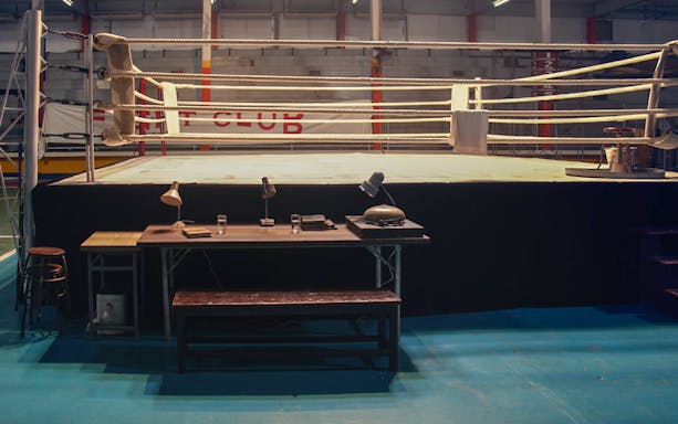 Boxing ring with desk and chairs in an indoor gym setting.