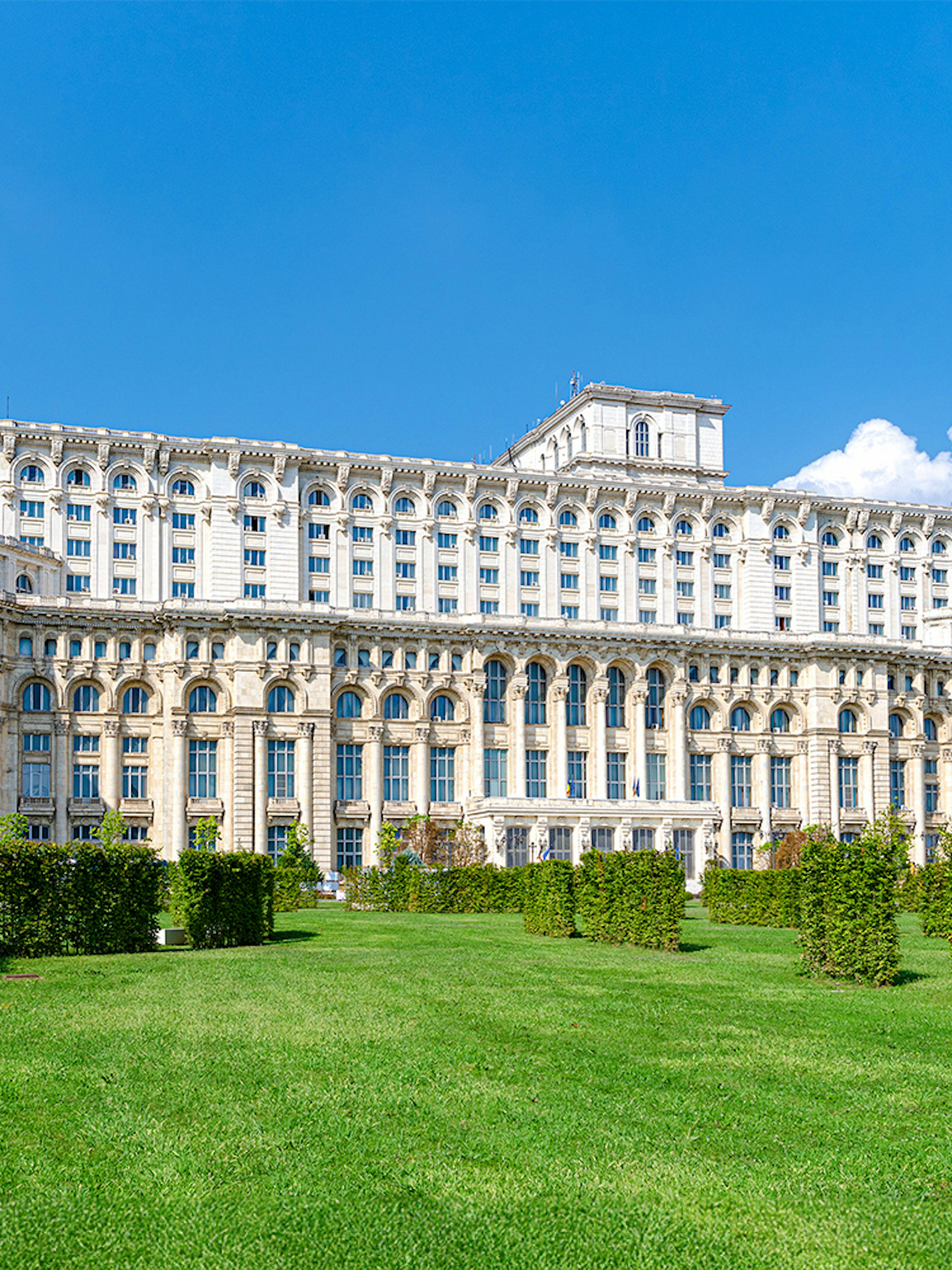 Palace of the Parliament in Bucharest with manicured gardens in the foreground.