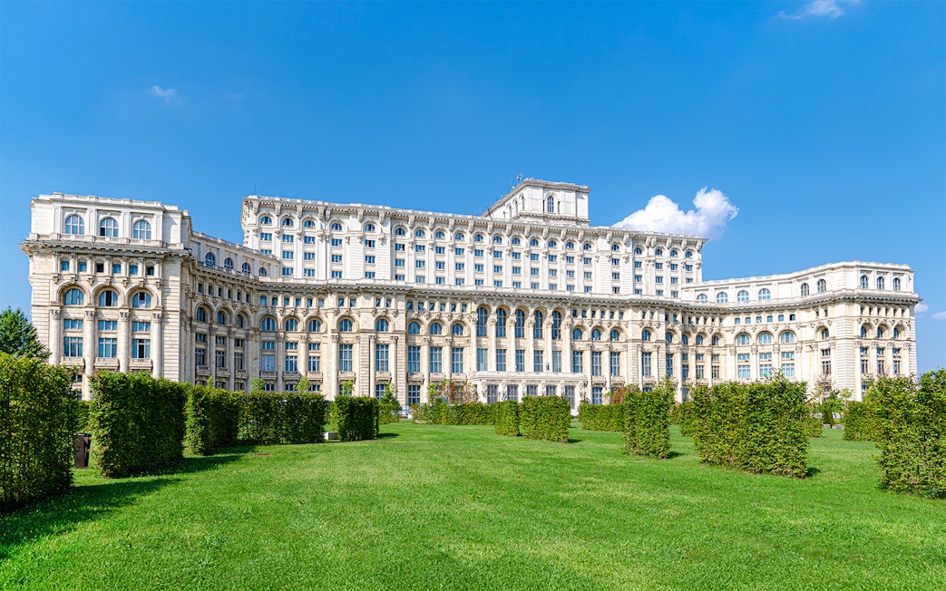 Palace of the Parliament in Bucharest with manicured gardens in the foreground.