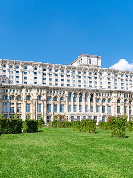 Palace of the Parliament in Bucharest with manicured gardens in the foreground.